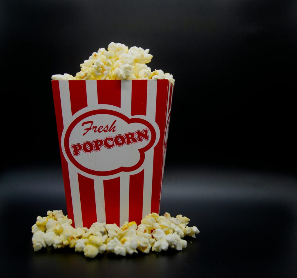 Close-up of freshly popped popcorn in a red and white striped box with black background.